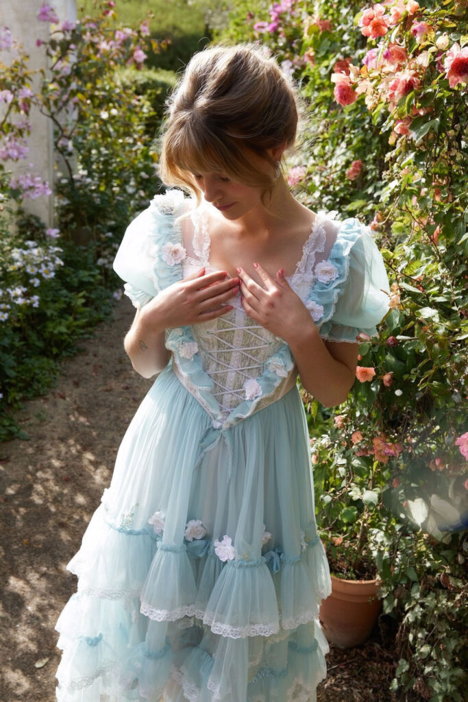 Woman wearing floral corsage on pastel dress, soft-focus floral background, warm light, Coquette Core style.