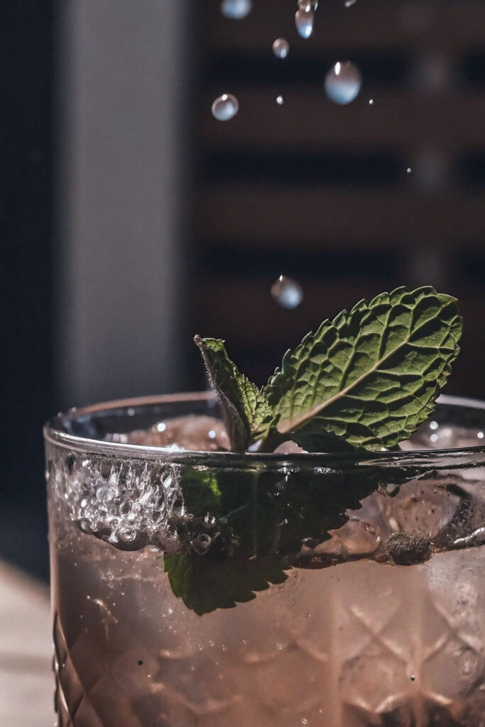 Fresh mint leaves dropping into sparkling water with ice, small splash and bubbles forming, glass with condensation, bright clean background, macro photography, refreshing summer aesthetic, natural daylight, droplets on glass surface"